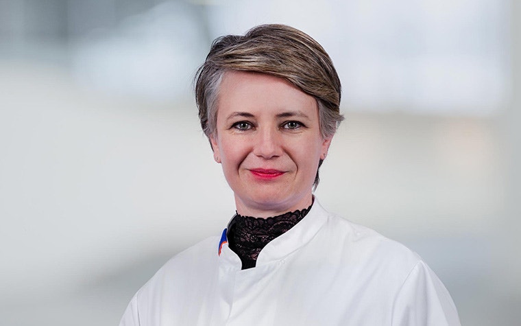 Dr. Joanna Wykrzykowska standing against a pale, blurred out background