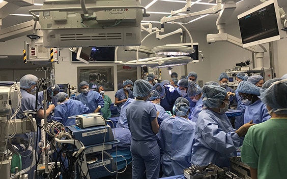 An operating room crowded with surgeons and clinicians wearing scrubs 