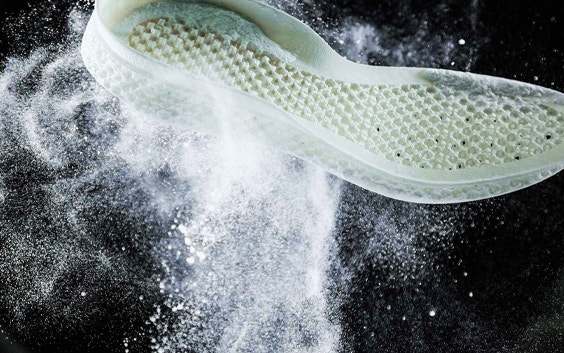 A 3D printed Adidas midsole is shown tossed up in mid-air surrounded by a cloud of white PA 12 powder. The midsole has a lattice structured base typical of laser sintering.