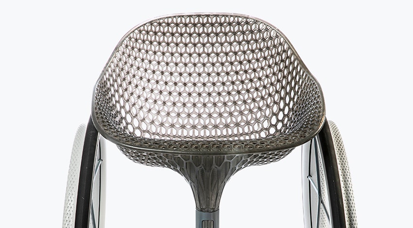 Frontal view of a 3D-printed prototype of a customized, futuristic-looking wheelchair, using multiple 3D printing materials. The seat is lattice-structured and made of a translucent gray resin. The foot-rest and wheel spokes are made of 3D-printed metal.