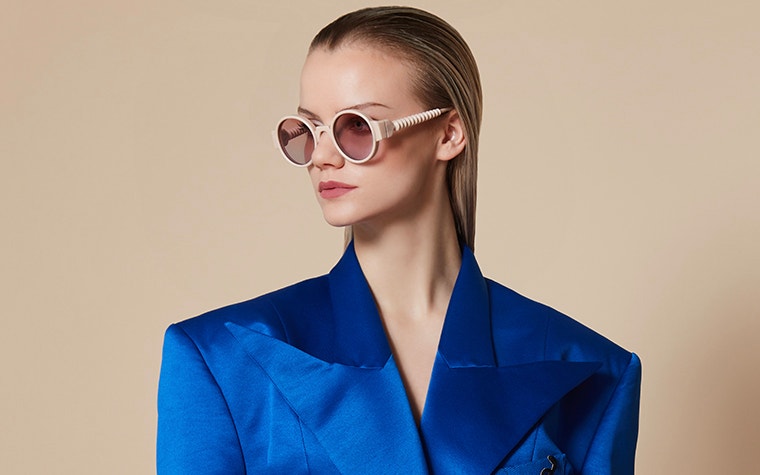 Weibliches Model in Blau, das eine nudefarbene Sonnenbrille von BAARS x Gogosha trägt und zur Seite schaut.