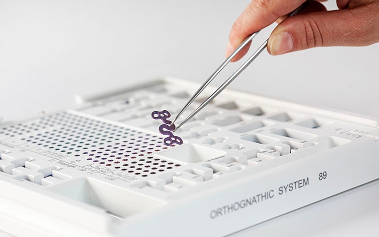 Hand using tweezers to pick up a 3D-printed piece from an orthognathic kit