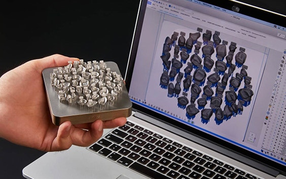 Persona che tiene in mano pezzi per odontotecnica stampati in 3D davanti a un laptop con Magics Dental Module in esecuzione