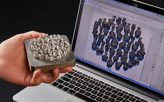 Person holding 3D-printed dental parts in front of a laptop with Magics Dental Module on it