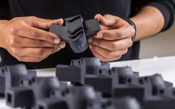 Le mani di un uomo che tengono una parte stampata in 3D in plastica nera.