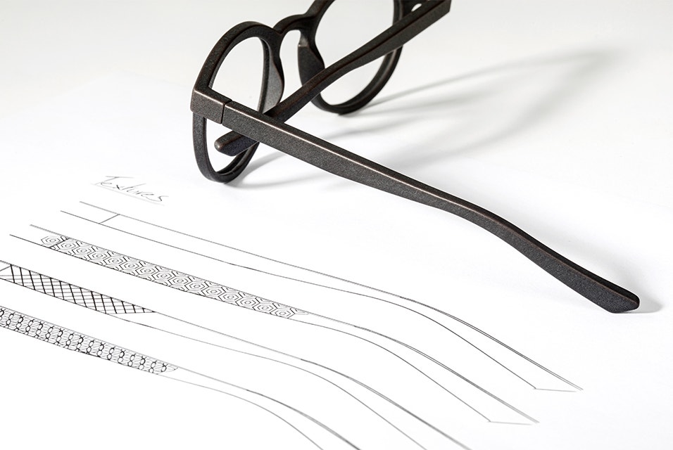 Montature per occhiali stampate in 3D posate sopra un foglio con progetti di aste per montatura