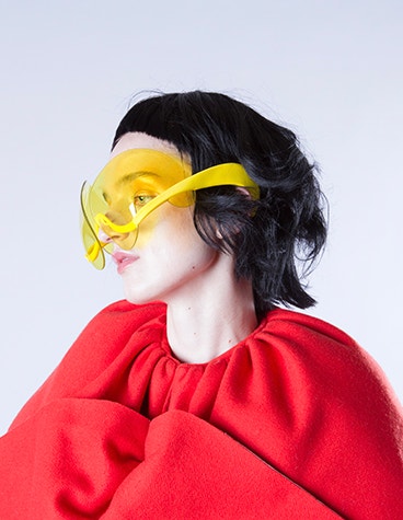 La modella indossa un abito rosso e occhiali da sole gialli e artistici disegnati da David Ring.