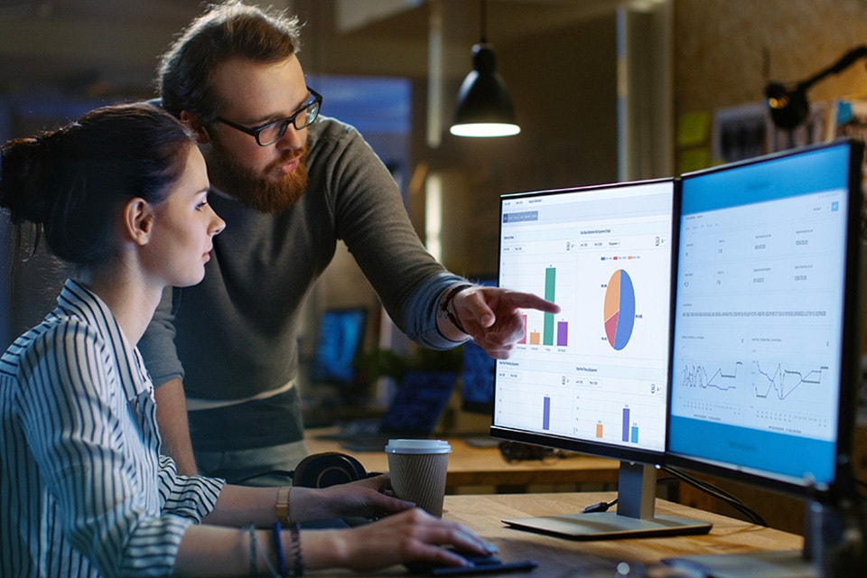 Two people at a desk looking at computer monitors with CO-AM software