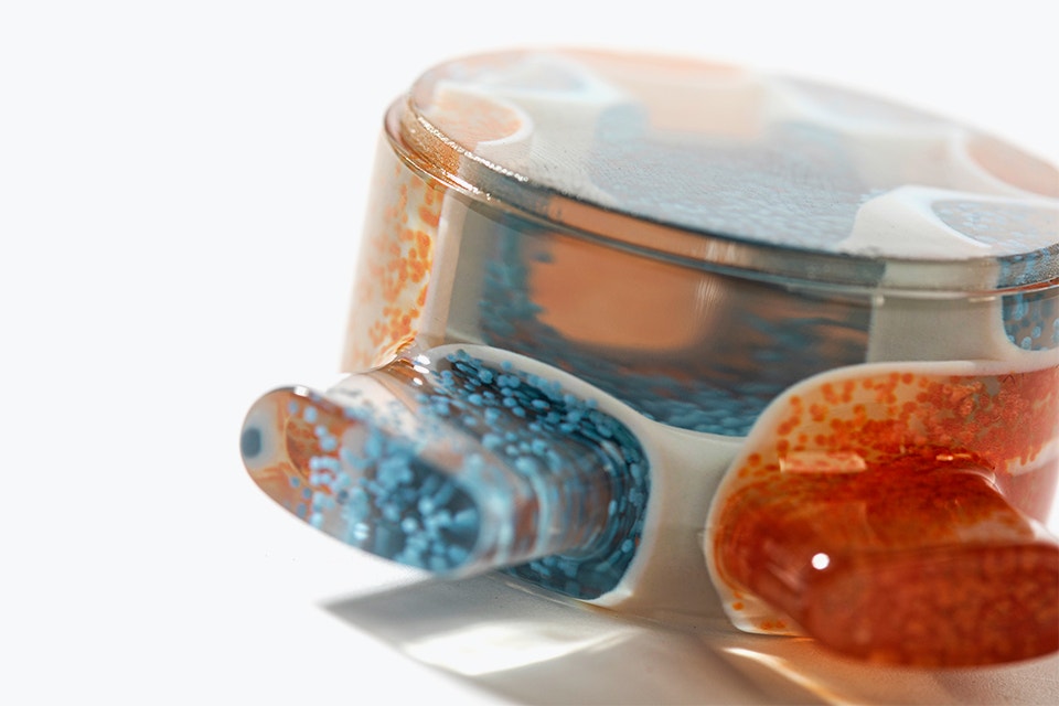 Vue rapprochée d'une pièce transparente imprimée en 3D avec des particules orange et bleues dispersées sur le côté