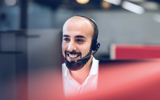 Operatore di assistenza clienti che indossa cuffie con microfono e sorride mentre osserva un computer