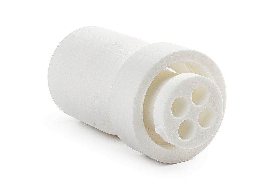 Una boquilla blanca impresa en 3D fabricada en poliamida 12 con cuatro orificios de extrusión. La boquilla se utiliza en una máquina de procesamiento de alimentos para producir malvaviscos de colores en una sola pieza, de Confiserie Van Damme.