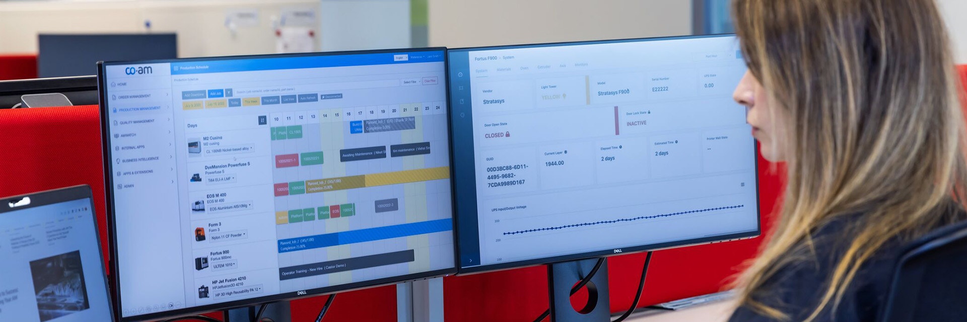 A woman sitting at a desk using three screens with the CO-AM Software Platform on display
