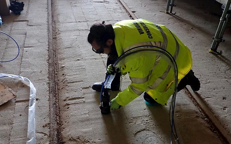 A Viridian consultant wearing a fluorescent vest, goggles, and gloves takes a reading from the ground using the sampling head 