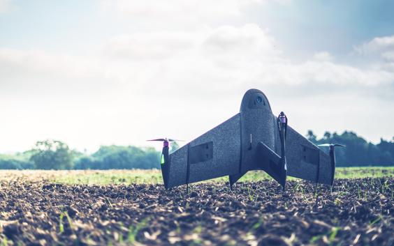 A 3D-printed surveying drone stands upright on a muddy field.