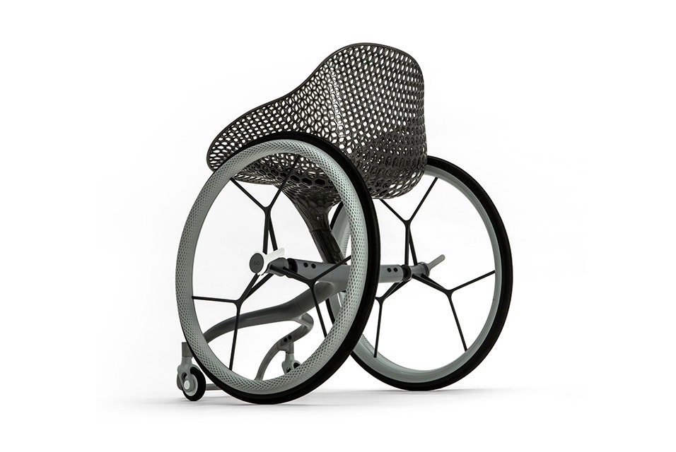 Backside view of a 3D-printed prototype of a customized, futuristic-looking wheelchair, using multiple 3D printing materials. The seat is lattice-structured and made of a translucent gray resin. The foot-rest and wheel spokes are made of 3D-printed metal. 

