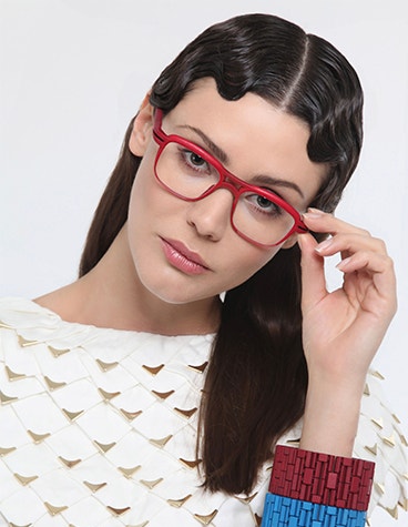 Female model with wavy hair holding red Hoet x Yuniku glass on her face and looking into the camera