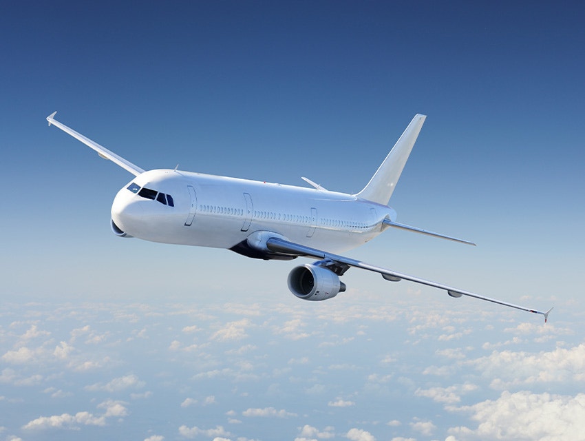 An unbranded commercial airplane flying against a blue sky with intermittent clouds.