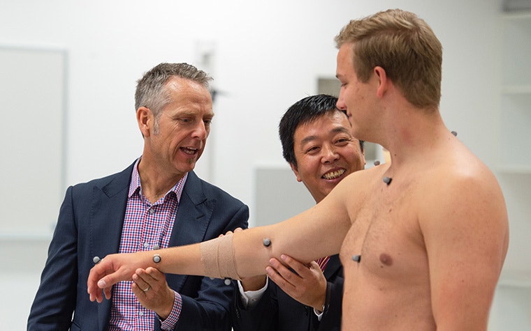 Two men check a patient's shoulder with multiple sensors on his body