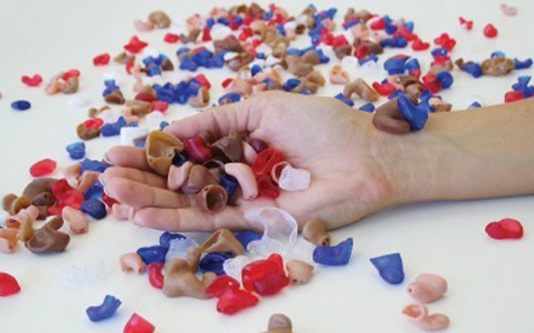 Hand holding many 3D-printed hearing aids on a table