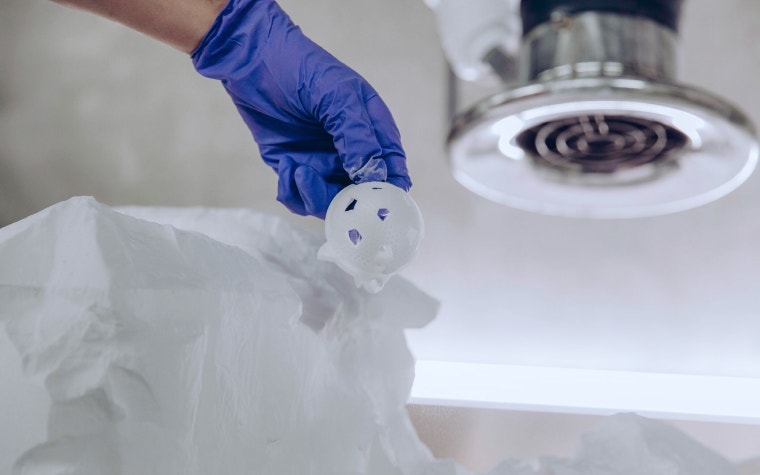 Gloved hand pulling a 3D-printed part out of a powder bed