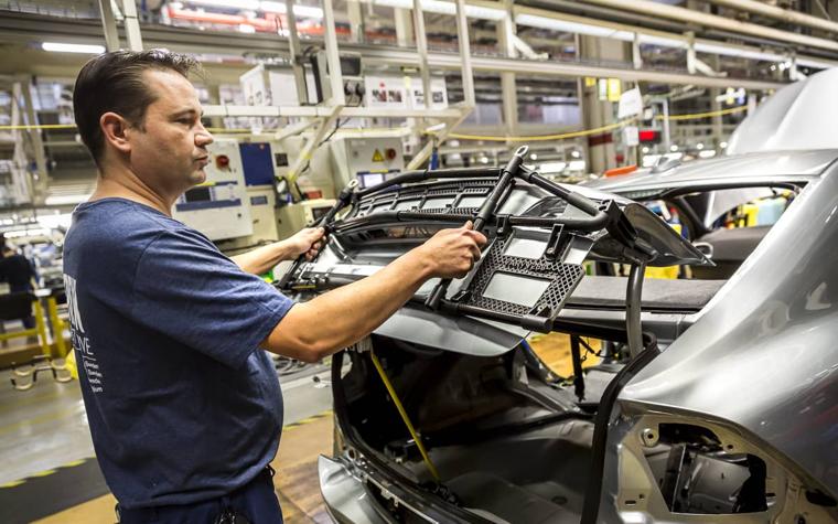 Man using a hand-held jig on a car in an automotive production