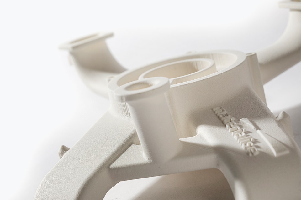 Detalle de un conducto de aire en blanco roto con múltiples aberturas curvadas, impreso en 3D con una poliamida sin halógeno y con retardante de llama.