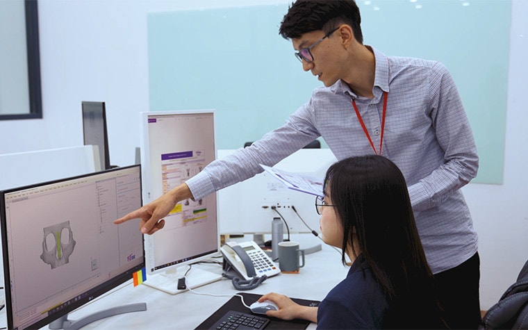 Man pointing to a computer with medical software while speaking to a woman sitting at a desk