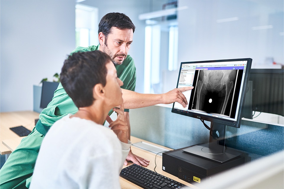 Man wearing scrubs is pointing to a computer screen with the OrthoView software next to a woman