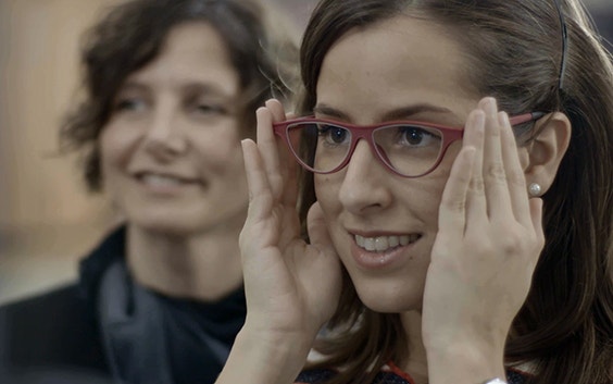 Customer trying on glasses with an optician watching in the background