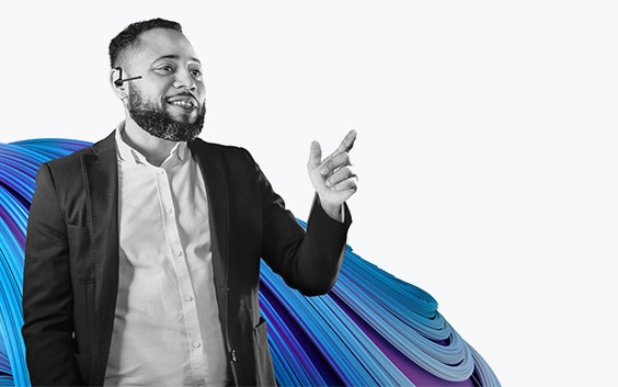 Man in a suit, pointing and smiling while wearing a headset, in black and white. The Mimics Innovation Suite signature blue and purple swirl is behind him