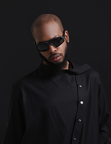 Modèle masculin noir, tout en noir, portant des lunettes de soleil de la collection Hoet Cabrio.