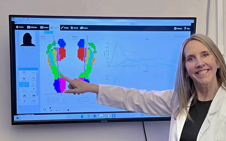 Dr. Jenny Sanders smiling and pointing to a screen with footscan software on it