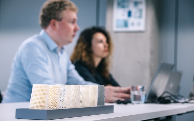 Focus on plastic, 3D-printed parts with two trainees sitting on their laptops in the background