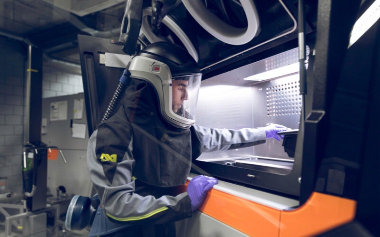 Operario de una máquina de impresión 3D en metal metiendo la mano en una impresora 3D