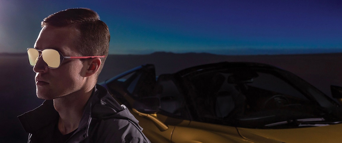 Model in front of a McLaren sports car wearing 3D-printed metal sunglasses from the McLaren Vision Collection