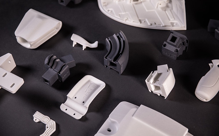 Eine Auswahl grauer und weißer 3D-gedruckter Polyamid-Bauteile auf schwarzem Filzgrund.