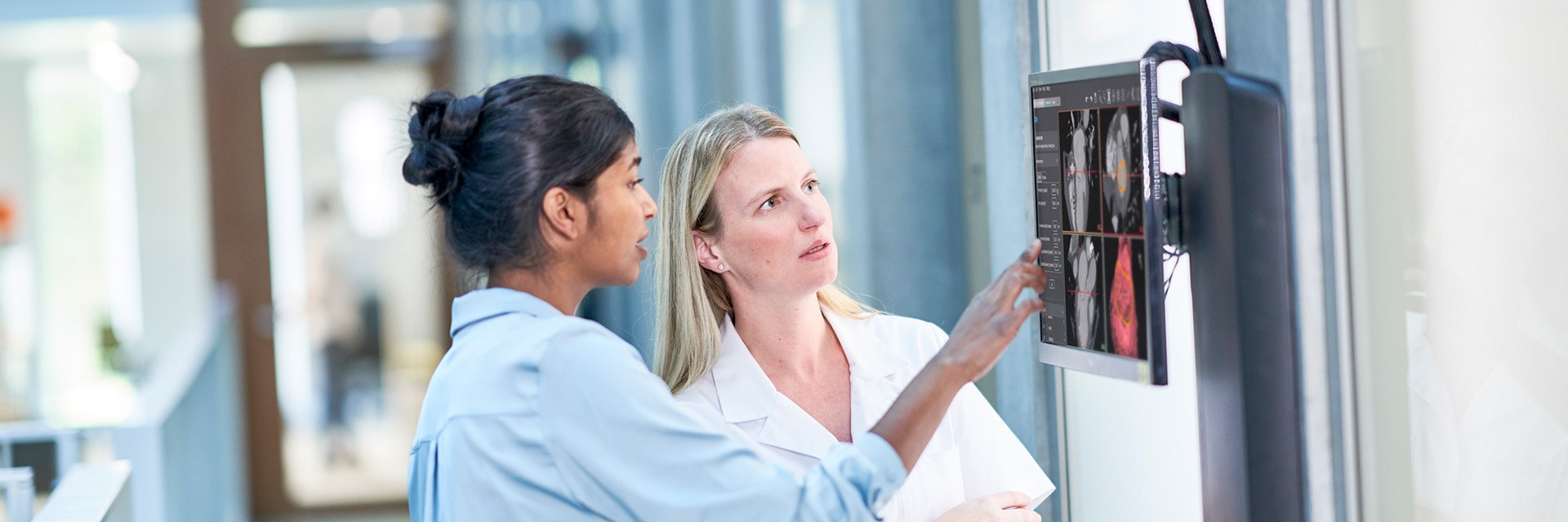 A medical technician and clinical engineer in a hospital hallway, looking at a monitor on the wall that displays Mimics