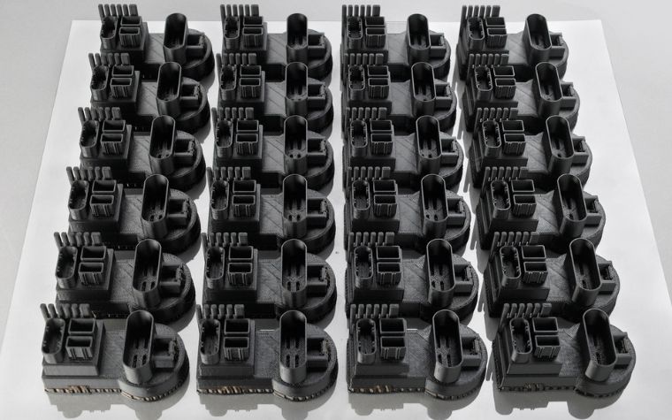 A row of identical 3D-printed parts made using FDM sitting on a white square.