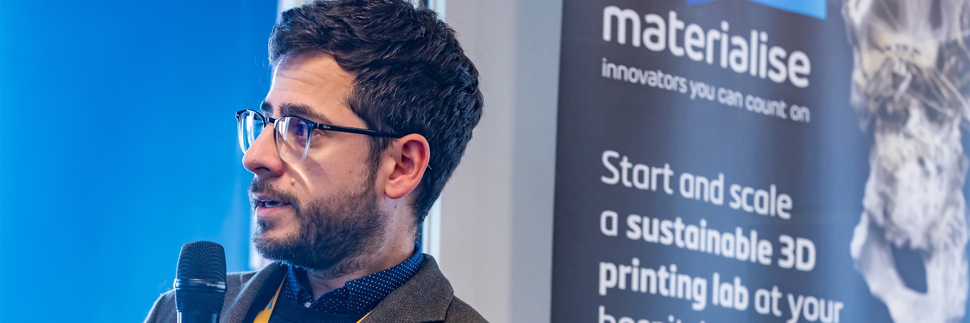 Ferran Fillat-Gomà speaks in front of a printed Materialise banner featuring text about starting and scaling a 3D-printing lab.