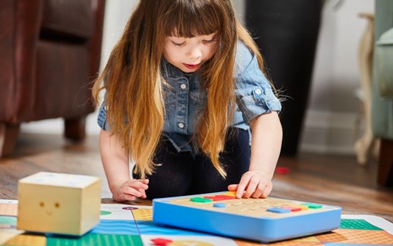 Bambino seduto su un pavimento in legno intento a giocare con il Cubetto Play Set di Primo Toys, che insegna ai più piccoli come programmare anche se non ancora in grado di leggere o scrivere.