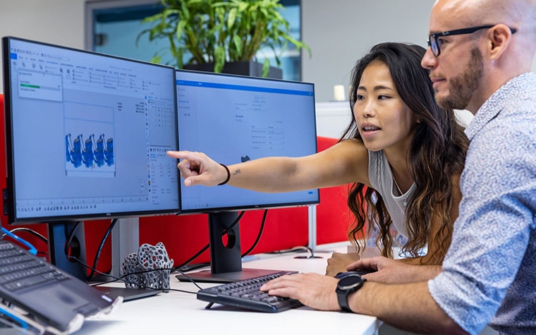 A woman pointing at a monitor while a male colleague is using 3D printing software