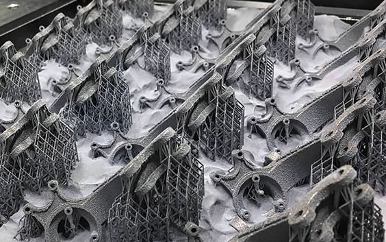 3D-printed metal parts with support structures, surrounded by loose powder