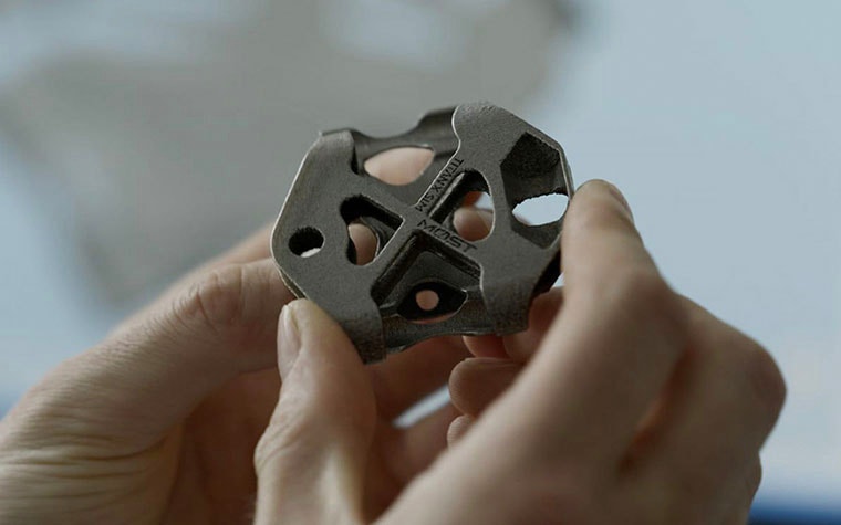 Hands holding a small metal 3D-printed part for a bicycle