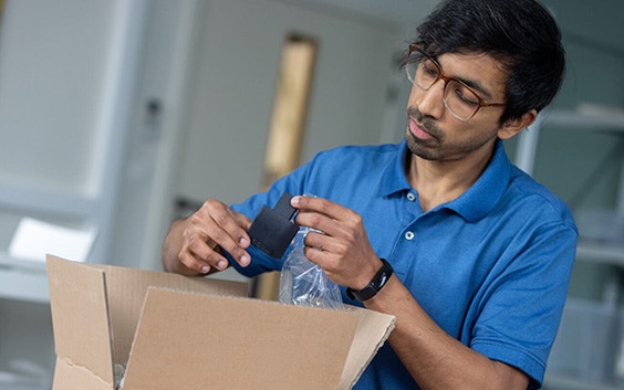 A man unboxes a small, black, 3D-printed part.