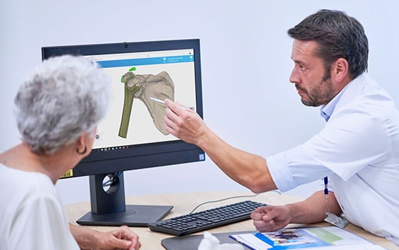 Doctor showing an elderly female patient a 3D digital model of a bone on a computer screen