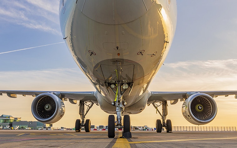 The nose of a large commercial aircraft sitting on a runway with a sunset in the background.
