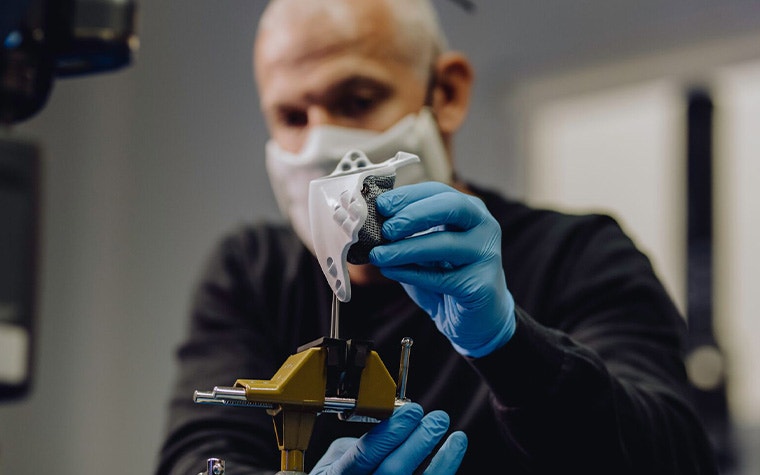 Ein Mann mit blauen Latexhandschuhen misst vorsichtig ein 3D-gedrucktes Teil aus