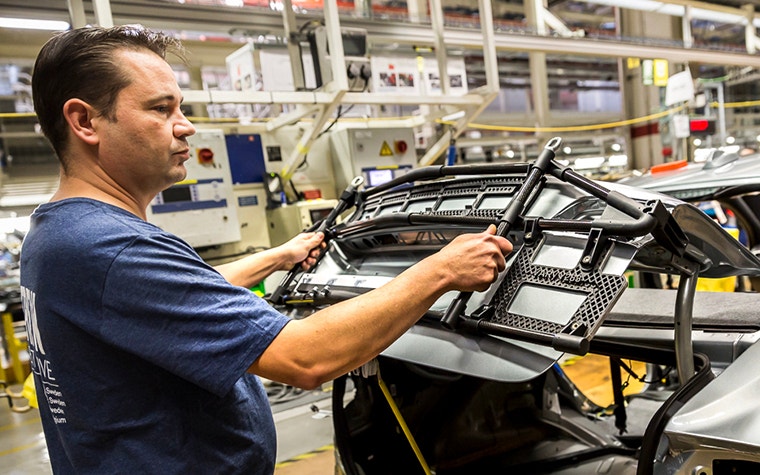 Werker einer Volvo-Fertigungslinie verwendet eine 3D-gedruckte Klebelehre an einem Auto in der Produktionslinie