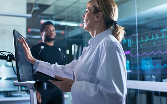 Frau, die auf einen Touchscreen in einem Forschungslabor drückt mit einem Patienten im Hintergrund