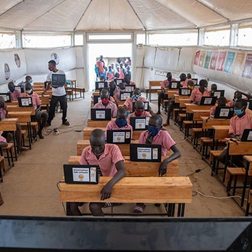 Children sitting at desks in a Maggie Shelter on computers
